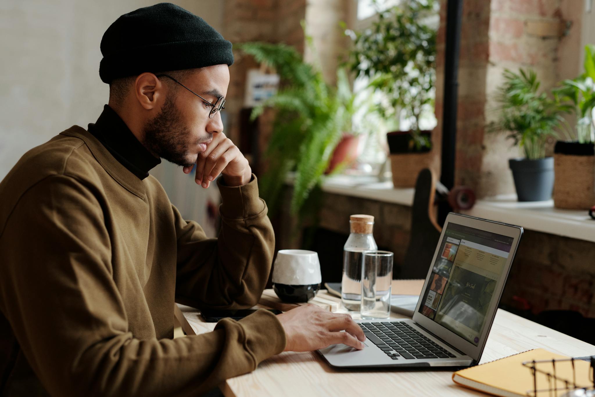 A stylish young man works remotely on his laptop in a cozy indoor workspace.