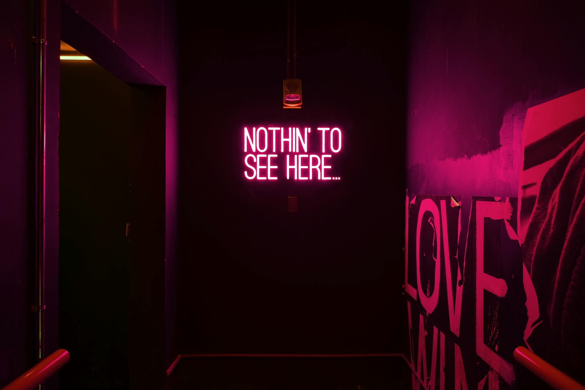 Neon sign reading 'Nothin' to see here...' in an artistic dark room.