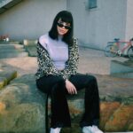 Stylish woman in animal print coat sits on a stone ledge in an urban setting, Bristol.