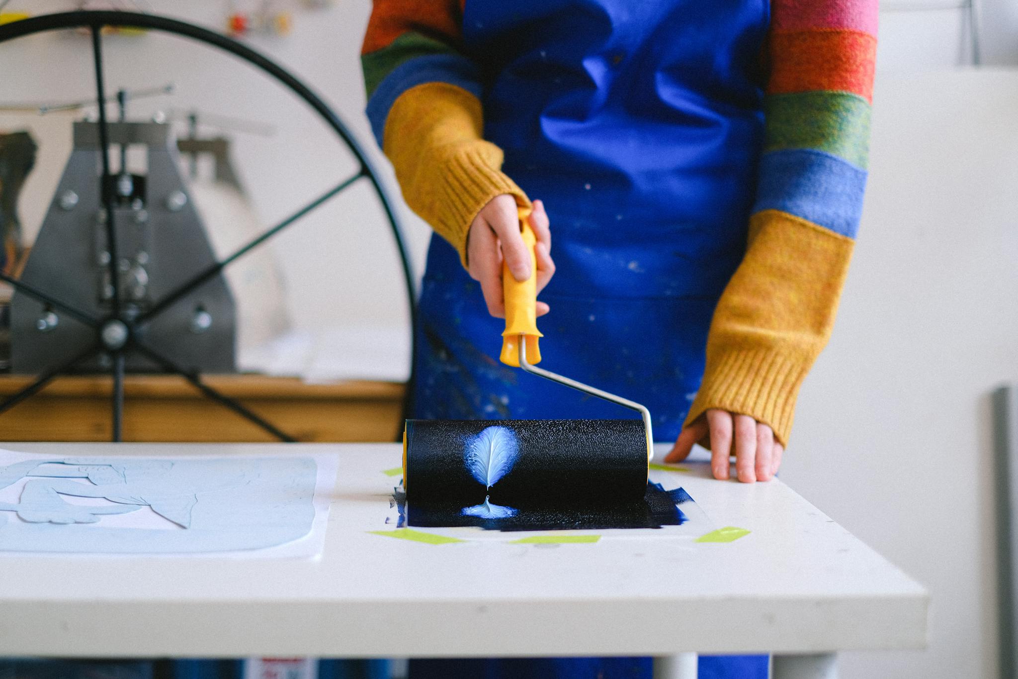 Woman using paint roller in art studio for creative crafting and design projects.